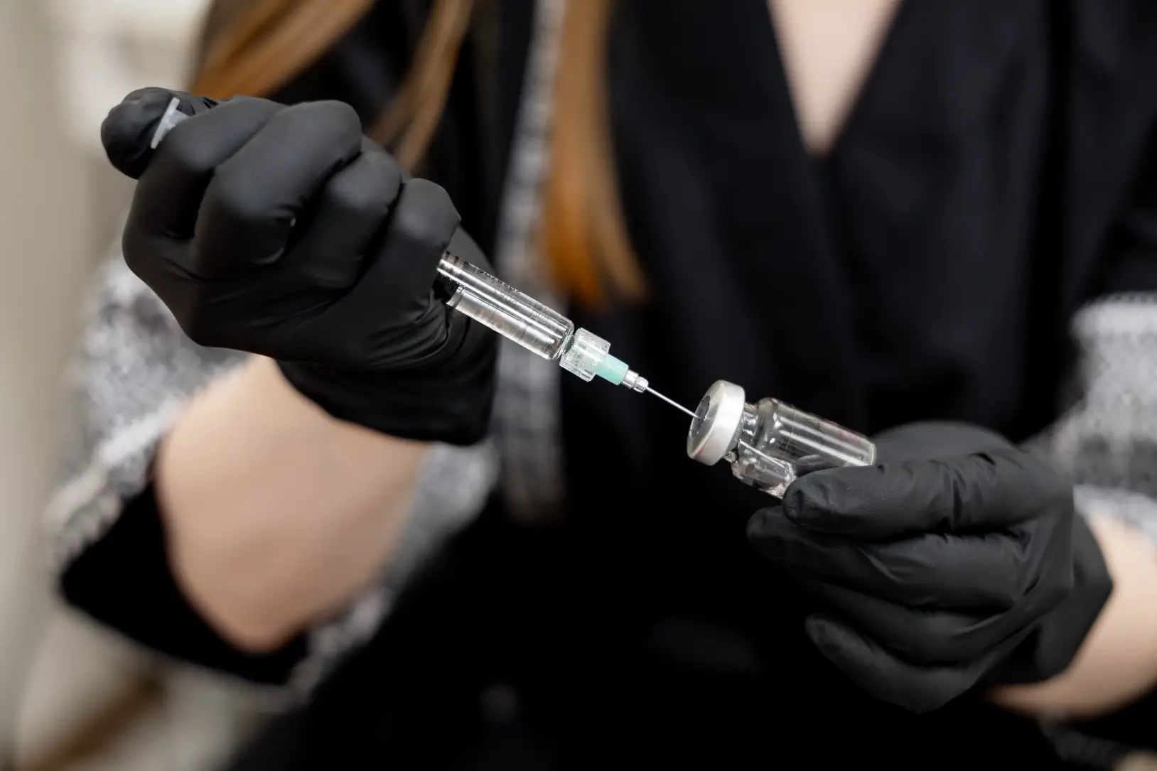 Gloved hands drawing liquid into syringe from vial