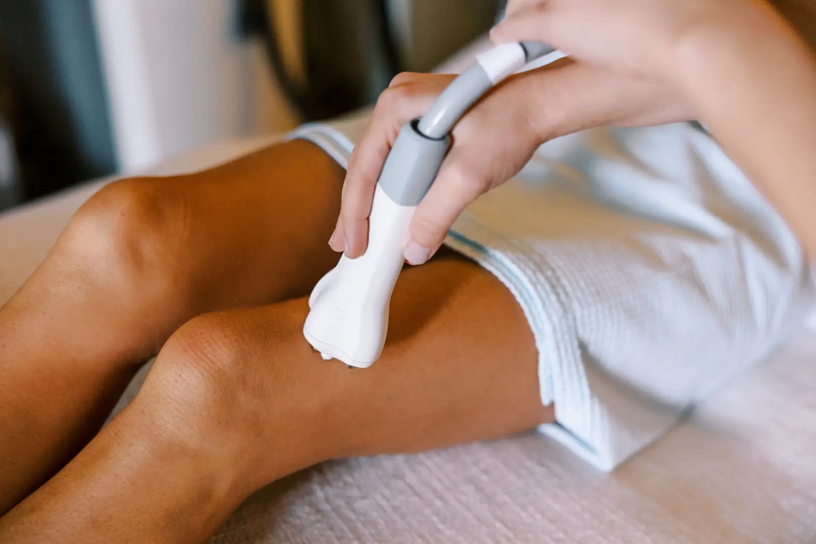 Practitioner using a handheld body contouring device on a person's thigh during a med spa treatment.