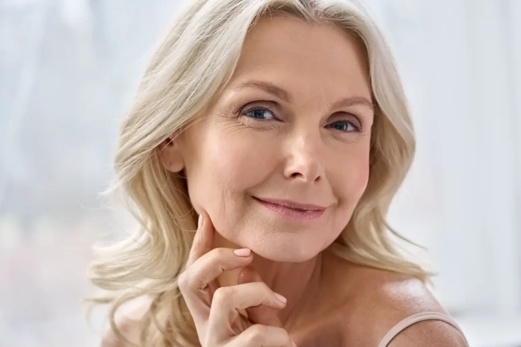 Mature woman touching her jawline while looking toward the camera in soft natural light.