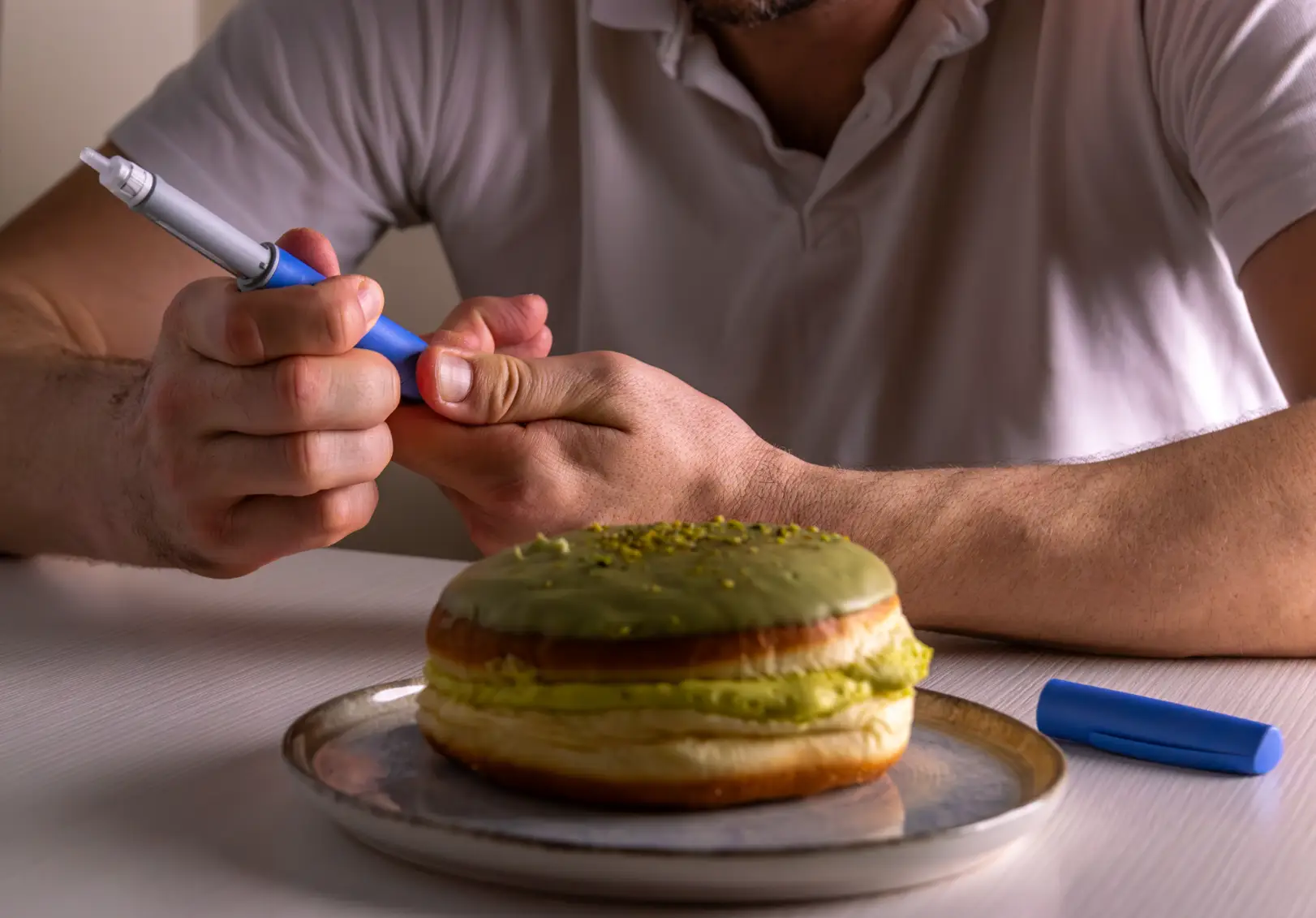 Man holding an injection pen near his abdomen with a dessert on a plate in front of him.